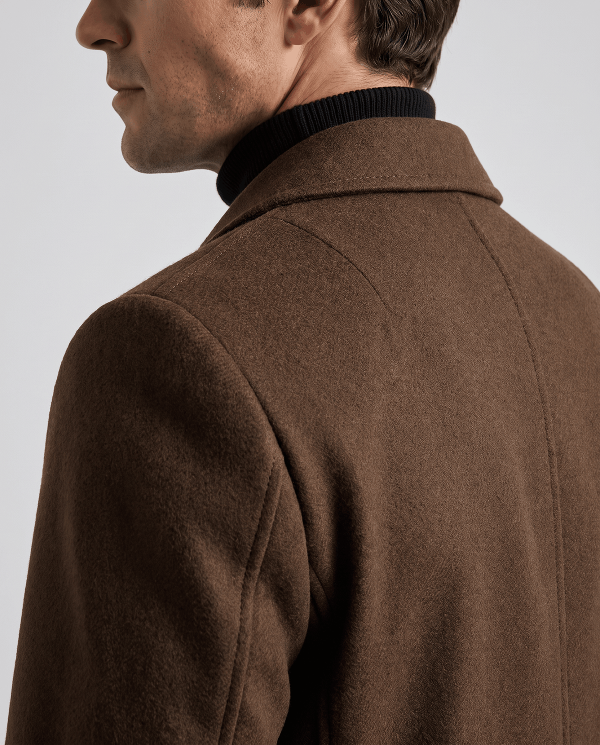 Rear close-up of the brown overcoat's collar and shoulder seam, worn over a turtleneck