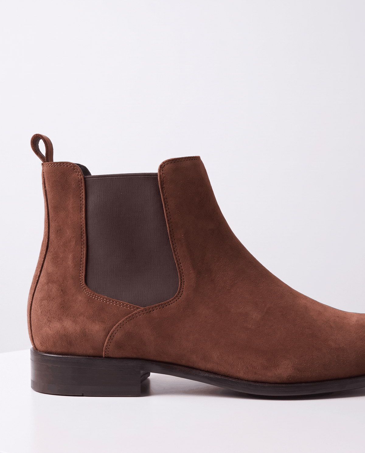 Side view of a brown suede boot with a dark elastic panel and heel pull tab