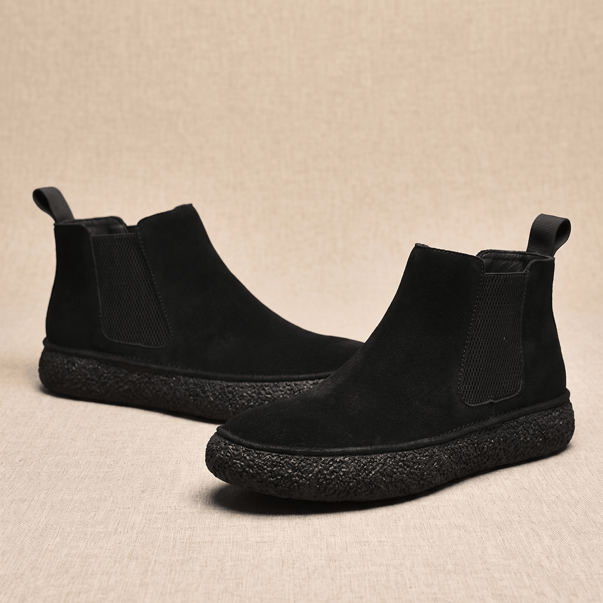 Pair of black suede Chelsea boots with elastic side panels, pull tabs, and thick crepe soles on a neutral background.