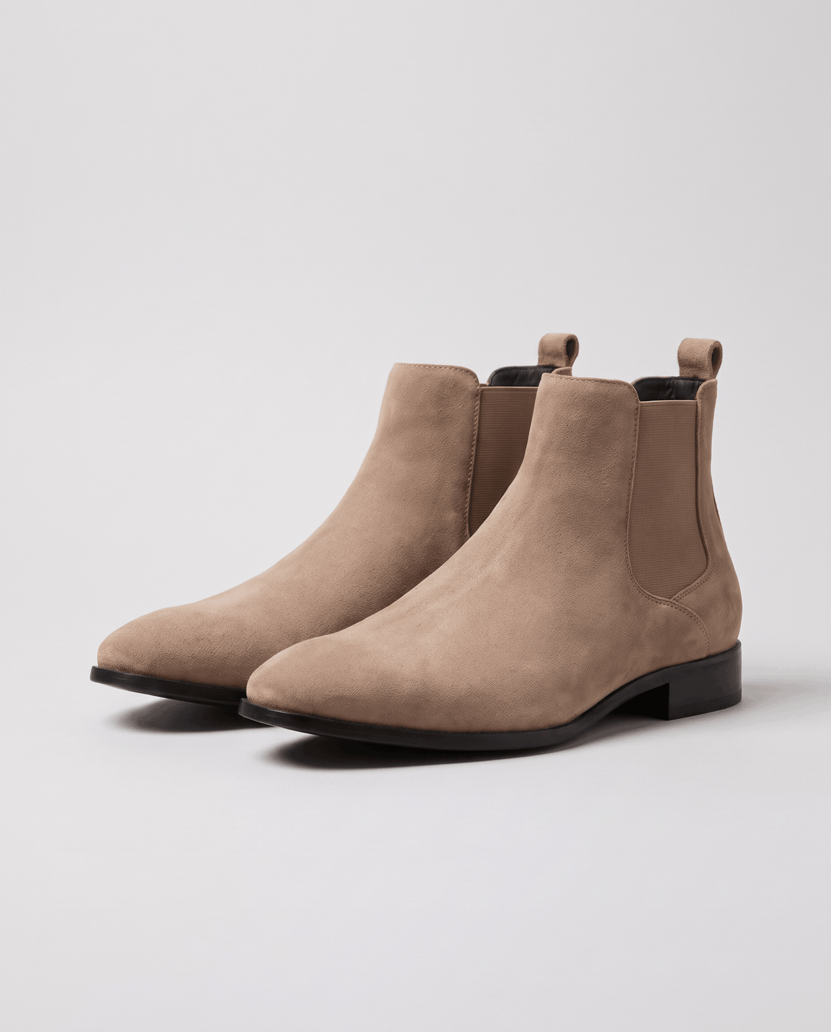 Pair of taupe suede slip-on boots with pull tabs on a pale background