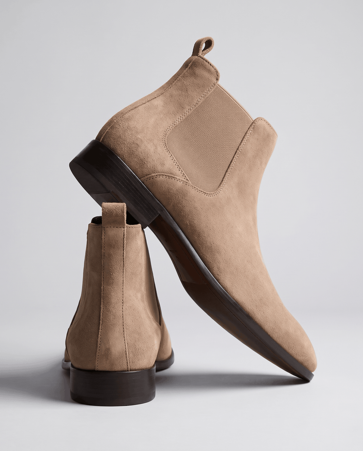 Taupe suede boot tilted to show the sole and heel, with a second boot beside it