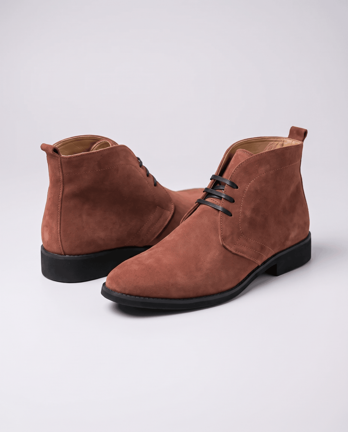 Brown suede chukka boots with dark laces and black sole shown at an angle.