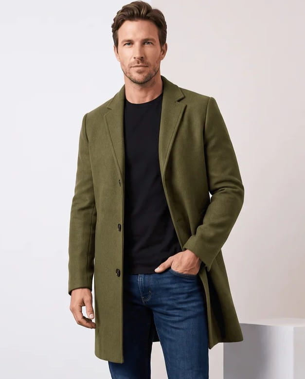 Men's tailored wool overcoat in army green with notch lapel, worn over a black tee and jeans