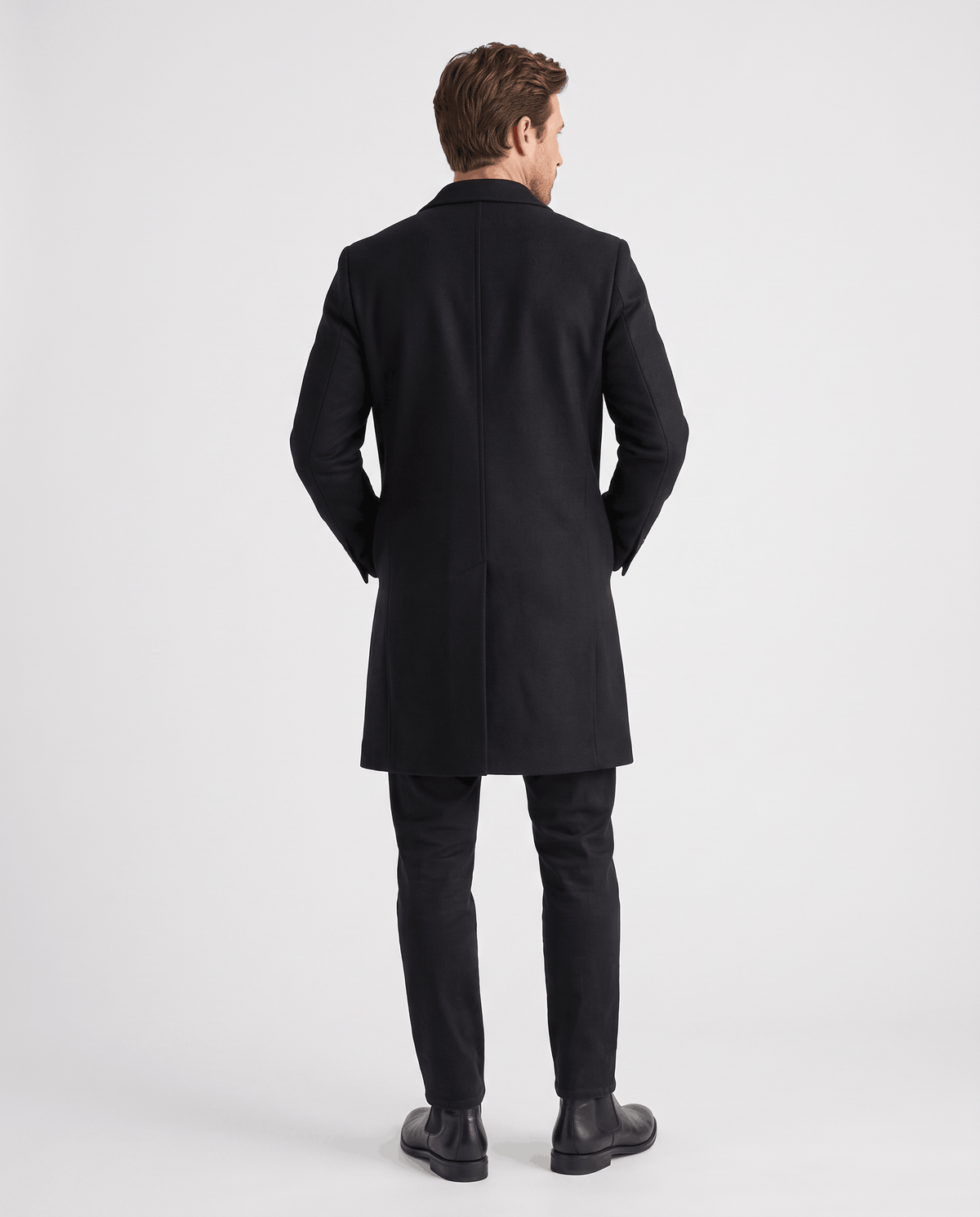 Back view of the black overcoat worn with black trousers and dress shoes