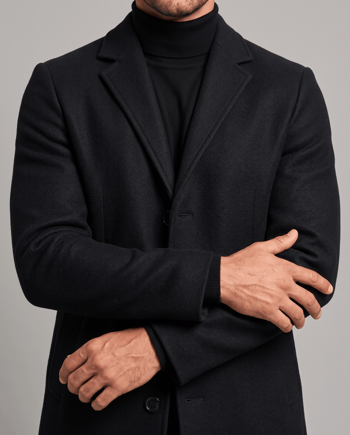 Black overcoat front detail with notch lapel and button front, worn with crossed arms