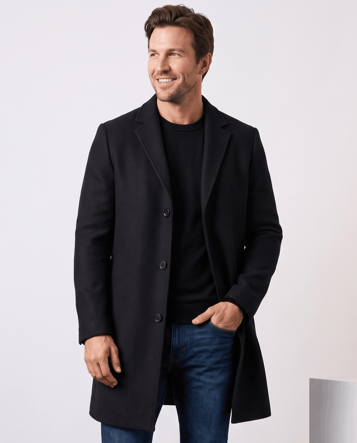 Black tailored overcoat with notch lapel, worn over a black tee with a hand in pocket