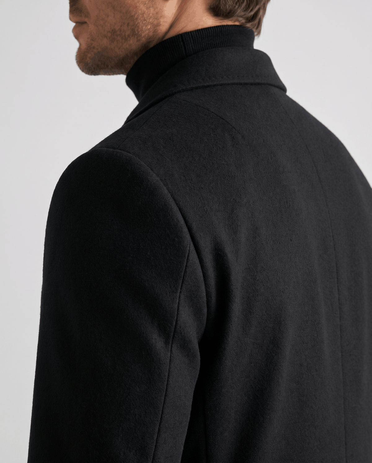 Side close-up of the black overcoat's collar and shoulder, worn over a black turtleneck