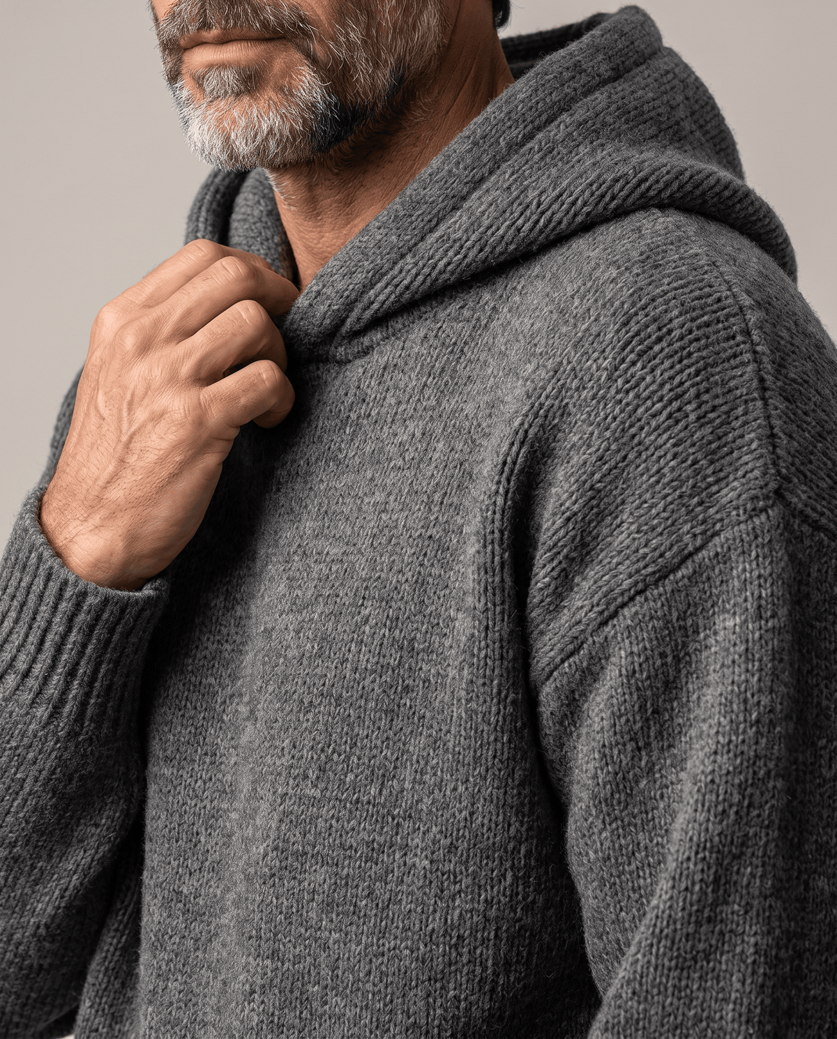 Side close-up of a dark gray knit hood with a hand resting at the collar