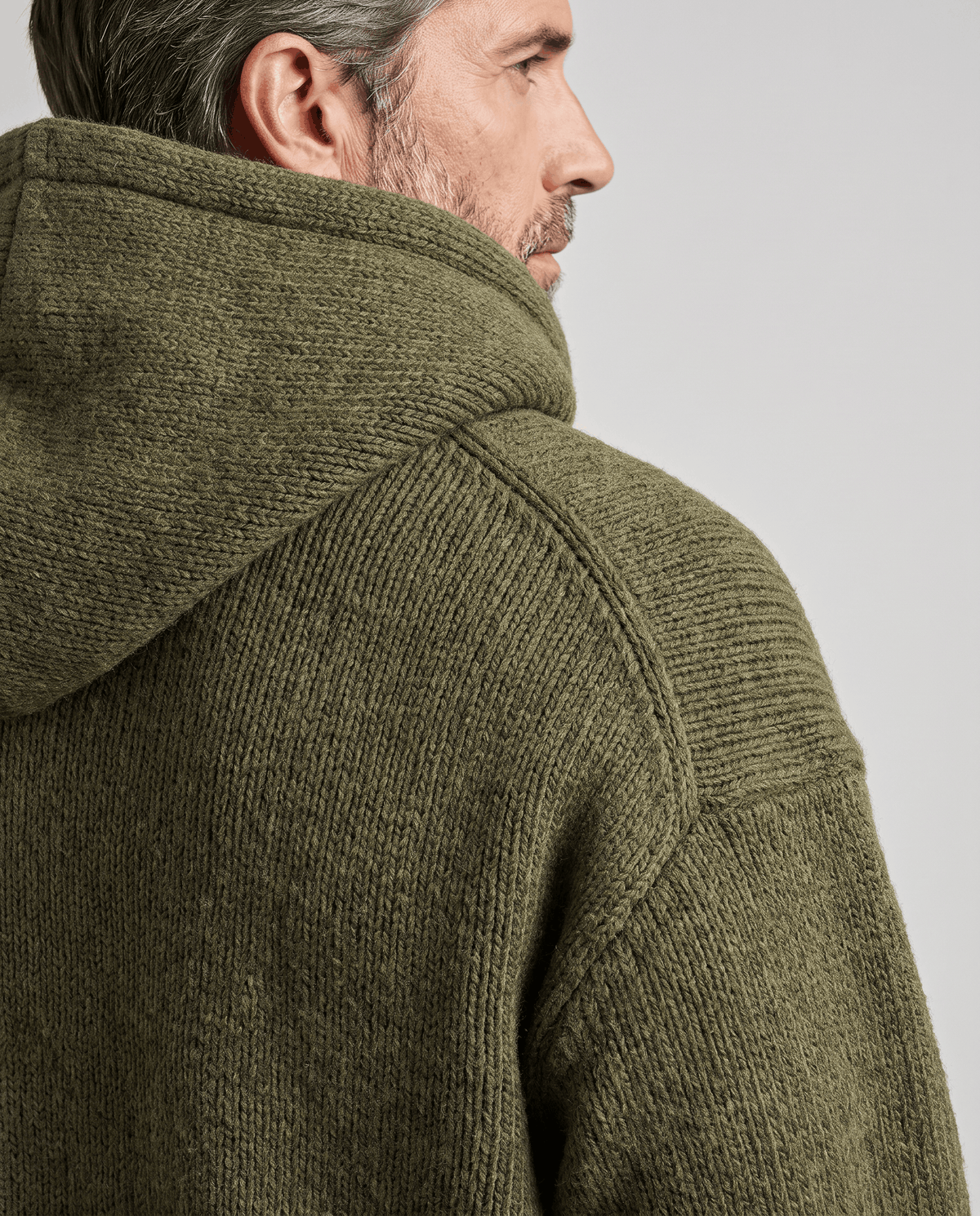 Side close-up of a green knit hood and shoulder seam on a wearer in profile