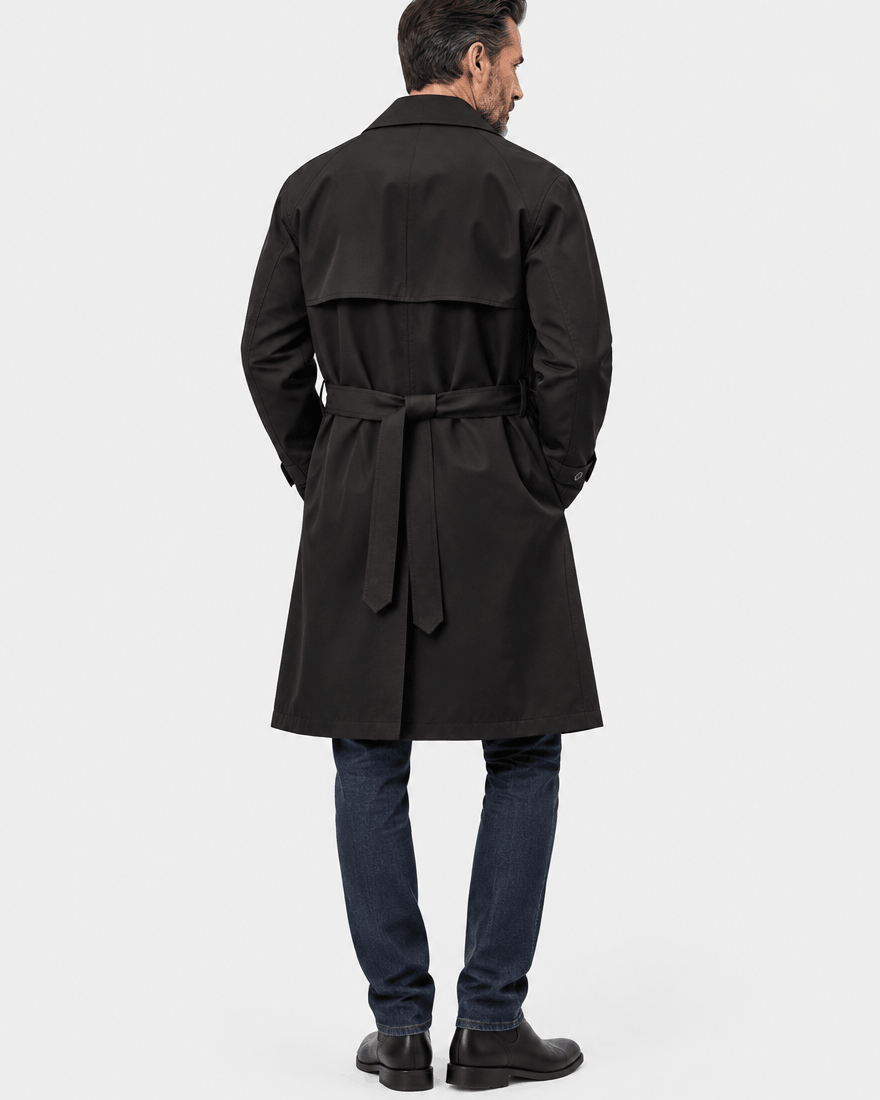 Back of the black longline coat showing the storm flap, belt tied at the waist and dark jeans