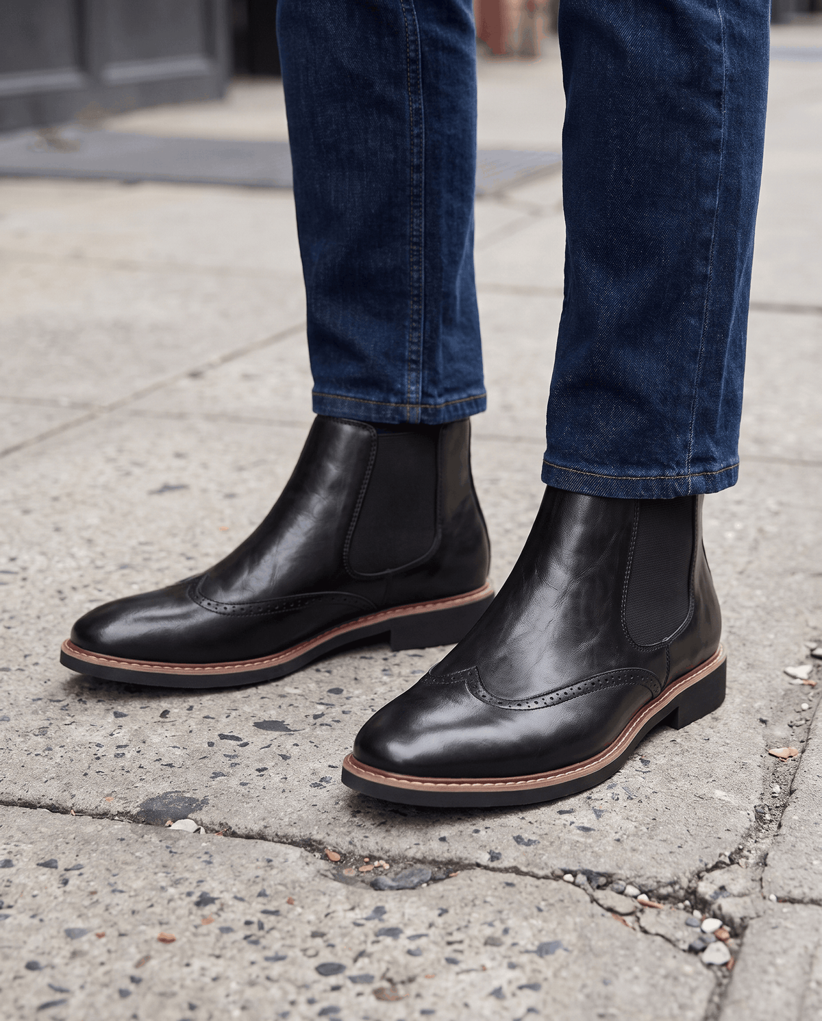 Black brogue boots worn with dark blue jeans on a paved sidewalk