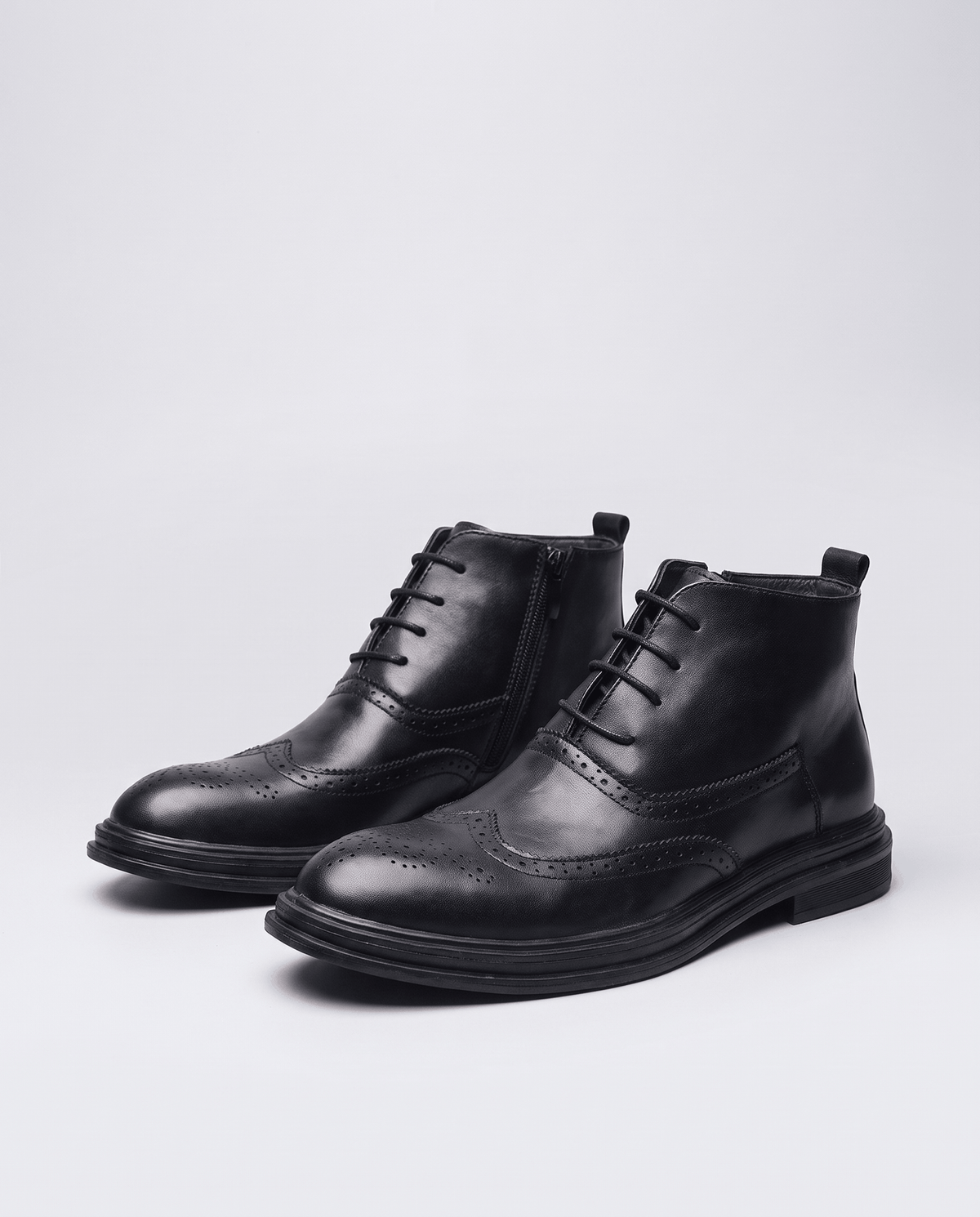 Pair of black lace-up brogue ankle boots on a light studio background