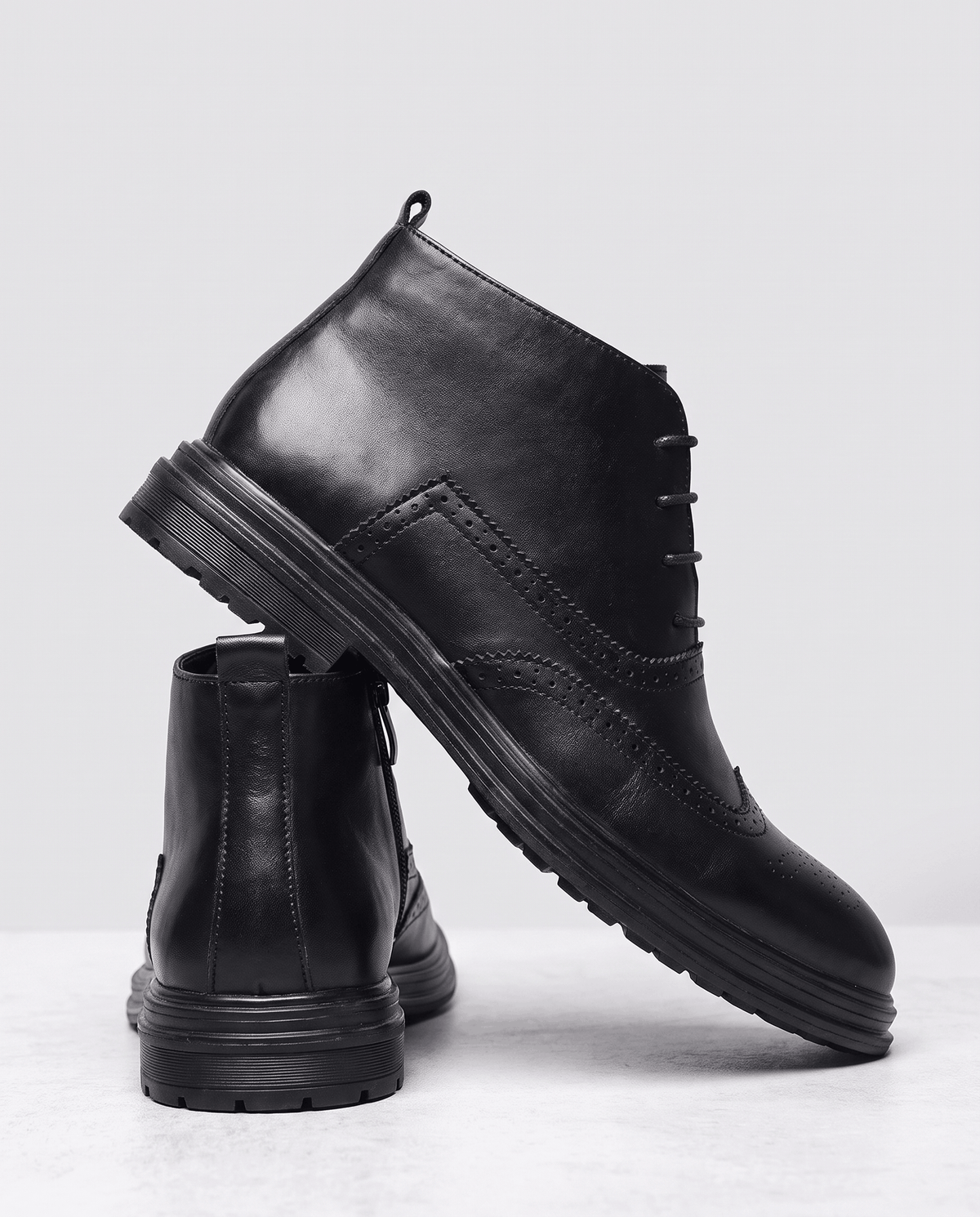 Black ankle boot tilted to show the sole, with a second boot standing behind