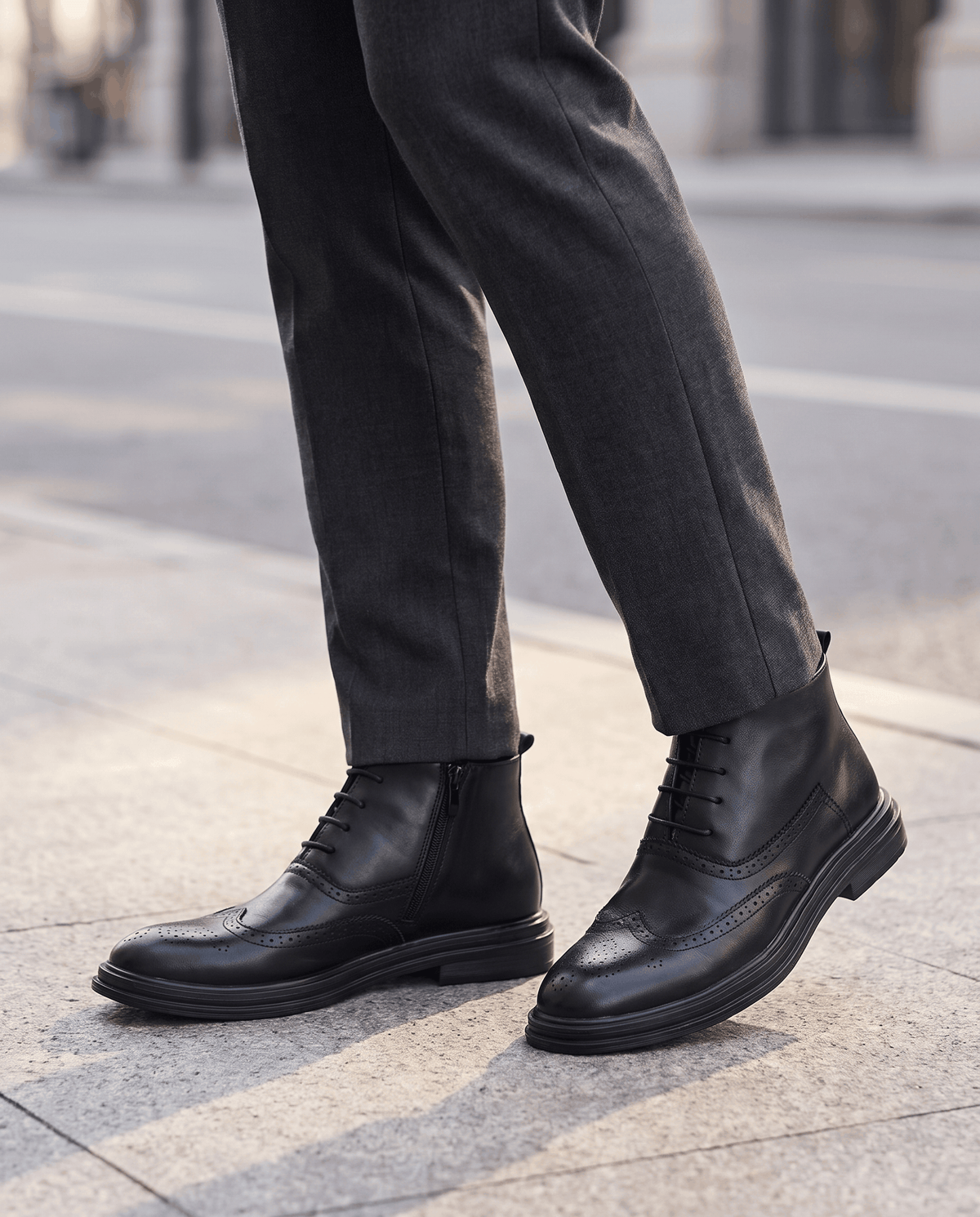 Man in black leather ankle boots and gray trousers standing on a city pavement