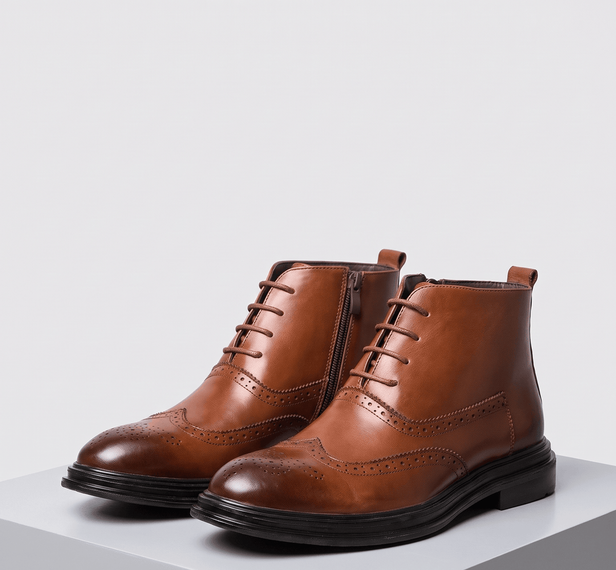 Brown brogue ankle boots side by side on a pale gray platform