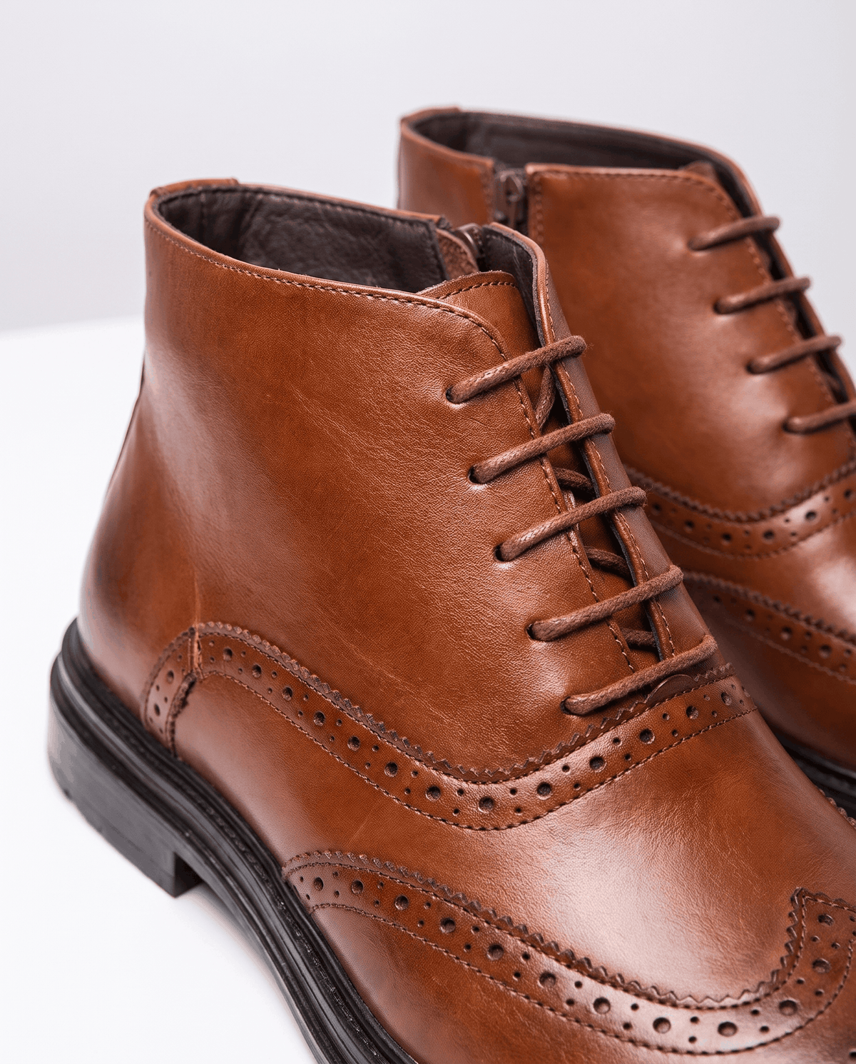 Close-up of brown brogue perforations, laces and side zip on a leather ankle boot