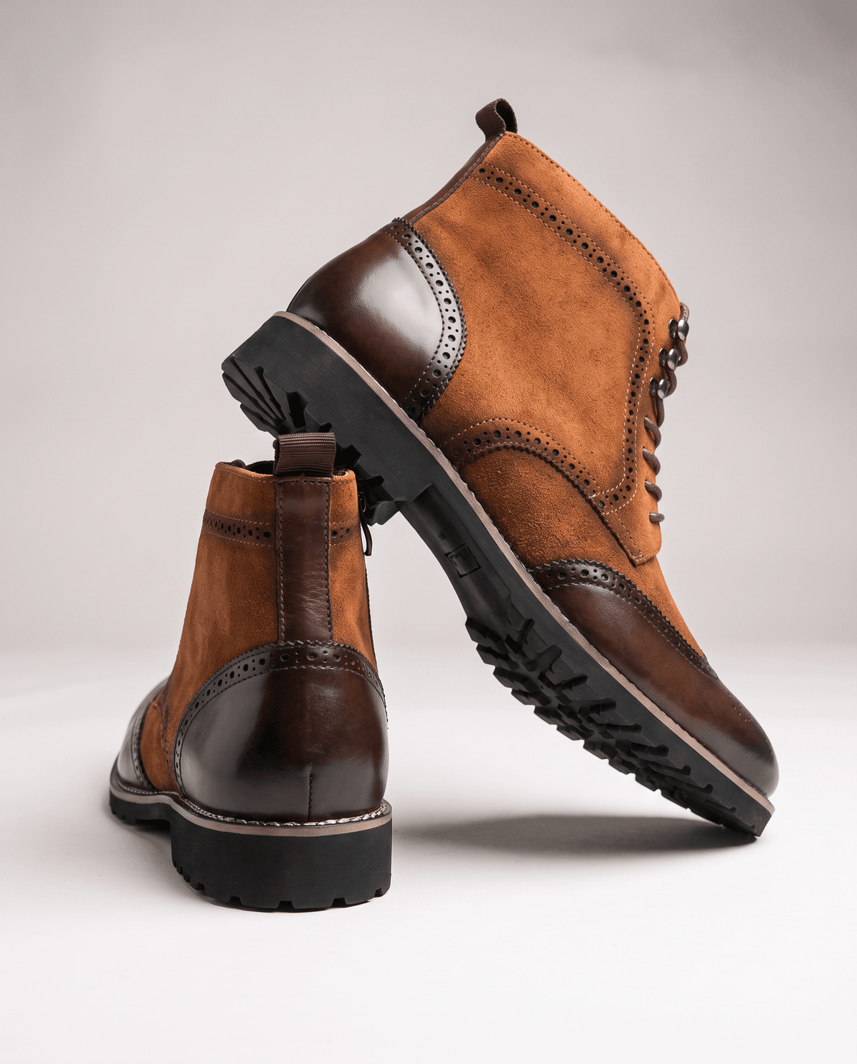 Brown wingtip boot tilted to show the rubber outsole, with a second boot behind