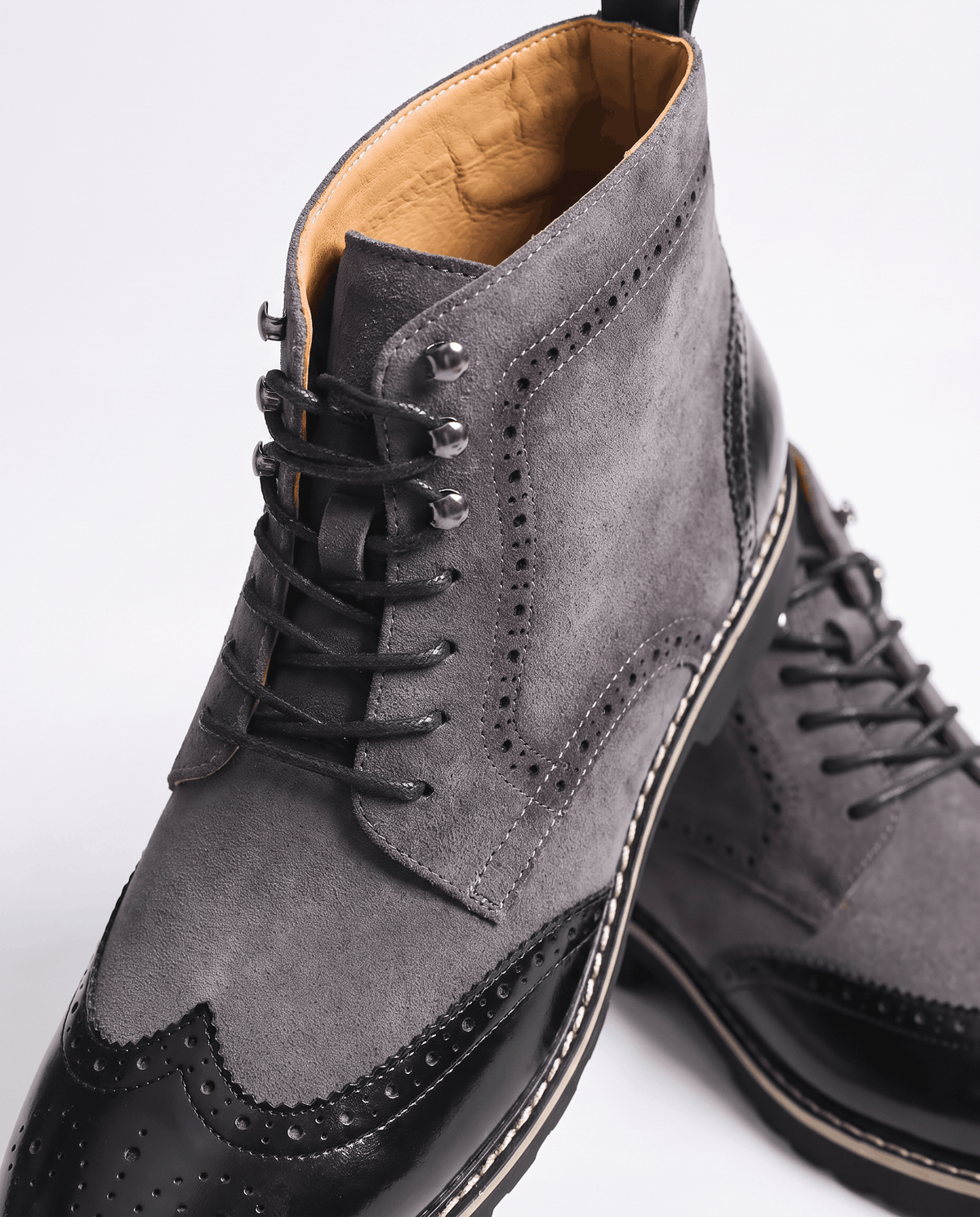 Close-up of gray suede boot with laces, tan lining and black wingtip toe