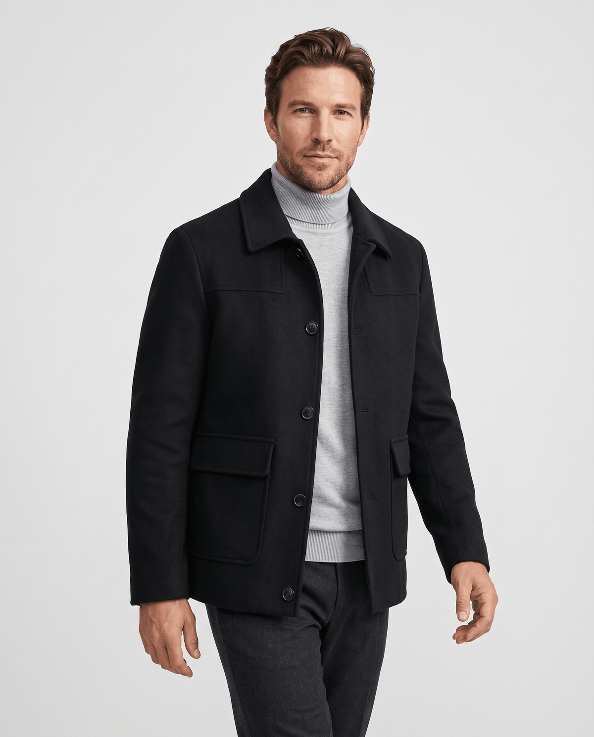 Black car coat worn open over a grey knit and dark trousers