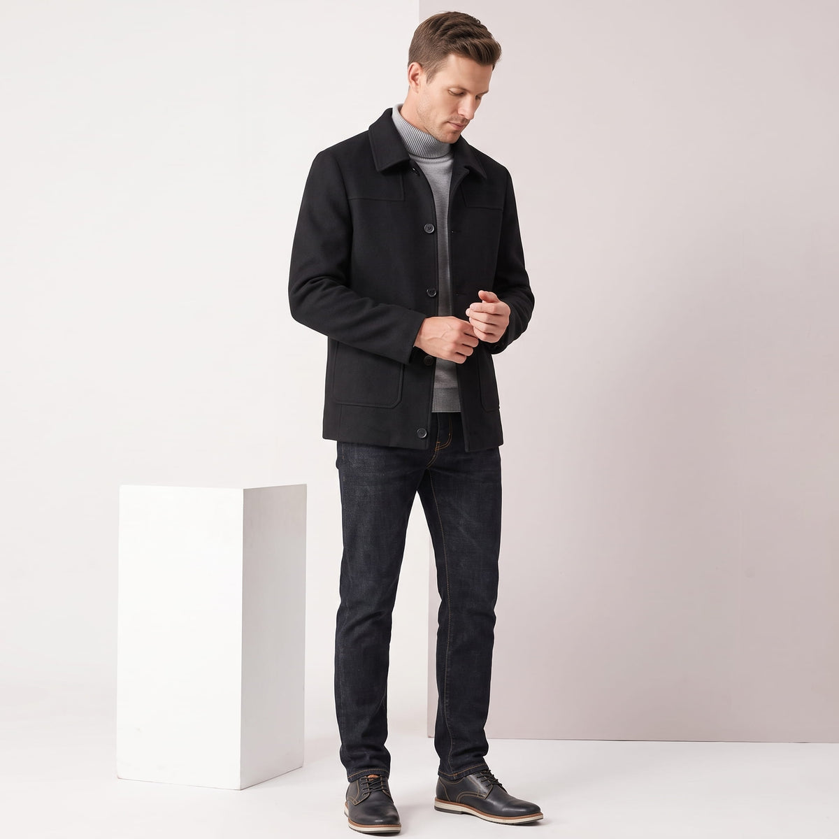 Full-length shot of the black coat worn beside a pale studio plinth