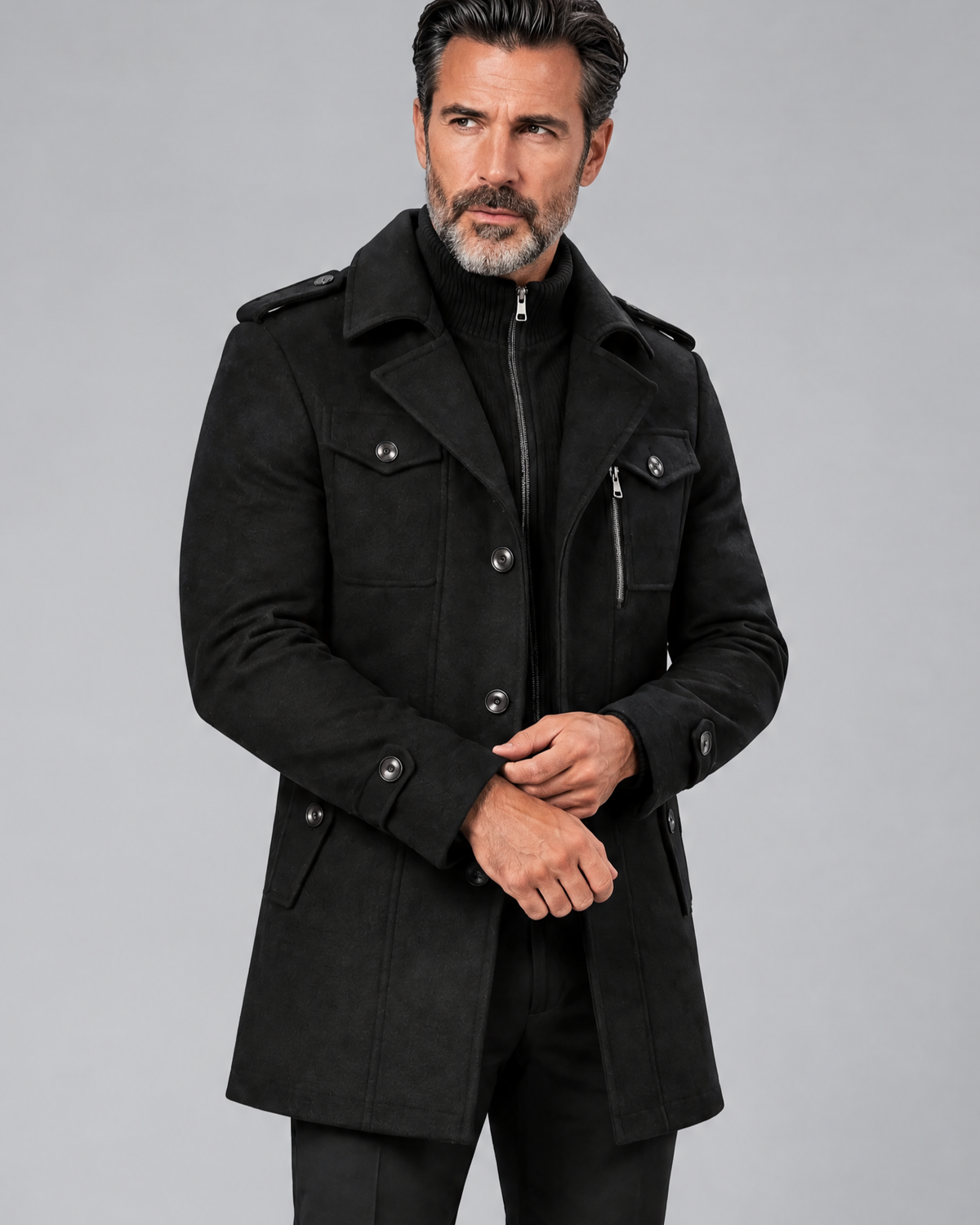 Black military-style coat with a knit bib at the neck, worn buttoned with hands clasped at the waist