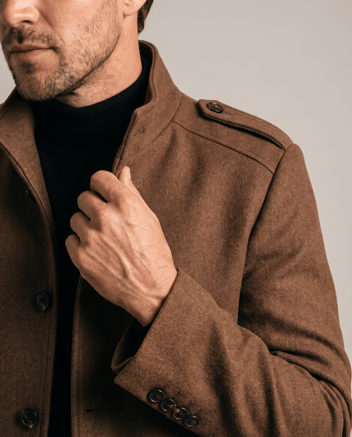 Brown overcoat collar and epaulette detail, with one hand at the button placket