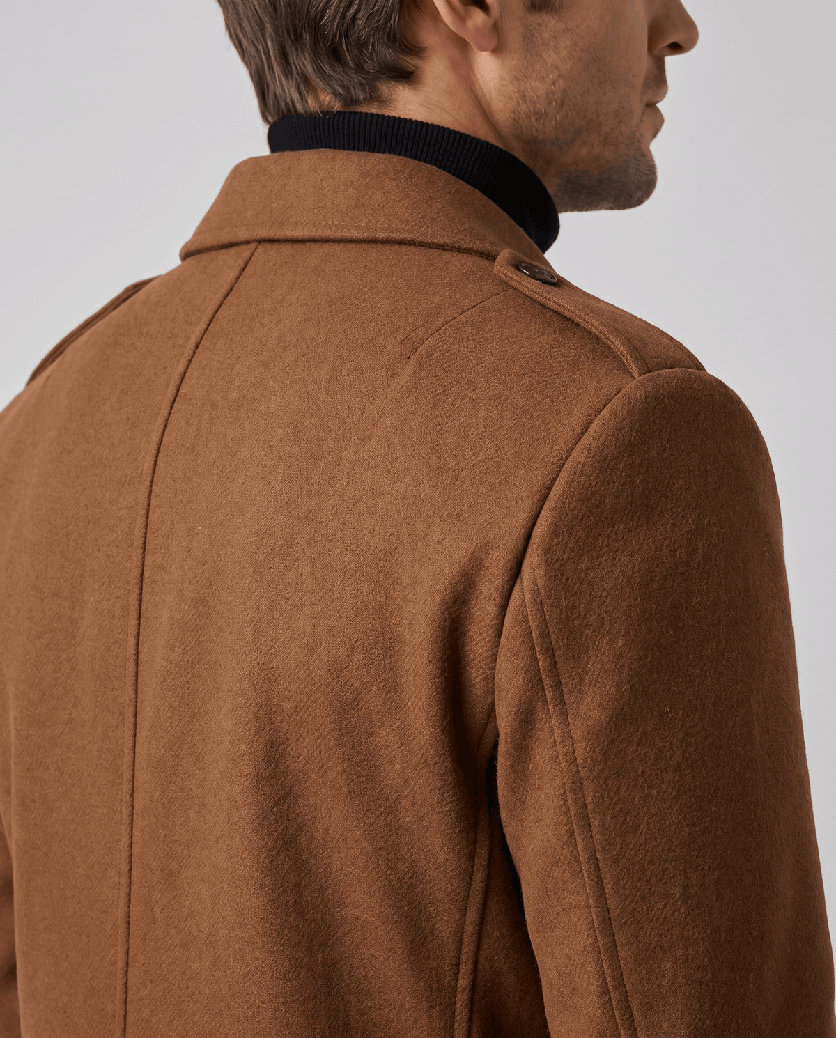 Close-up of the brown overcoat's smooth shoulder and collar, seen from the side