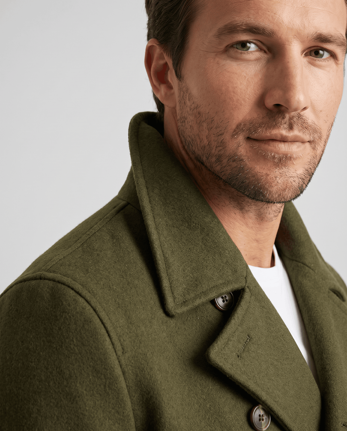 Close-up of wide notch lapel and button detail on an olive green wool coat