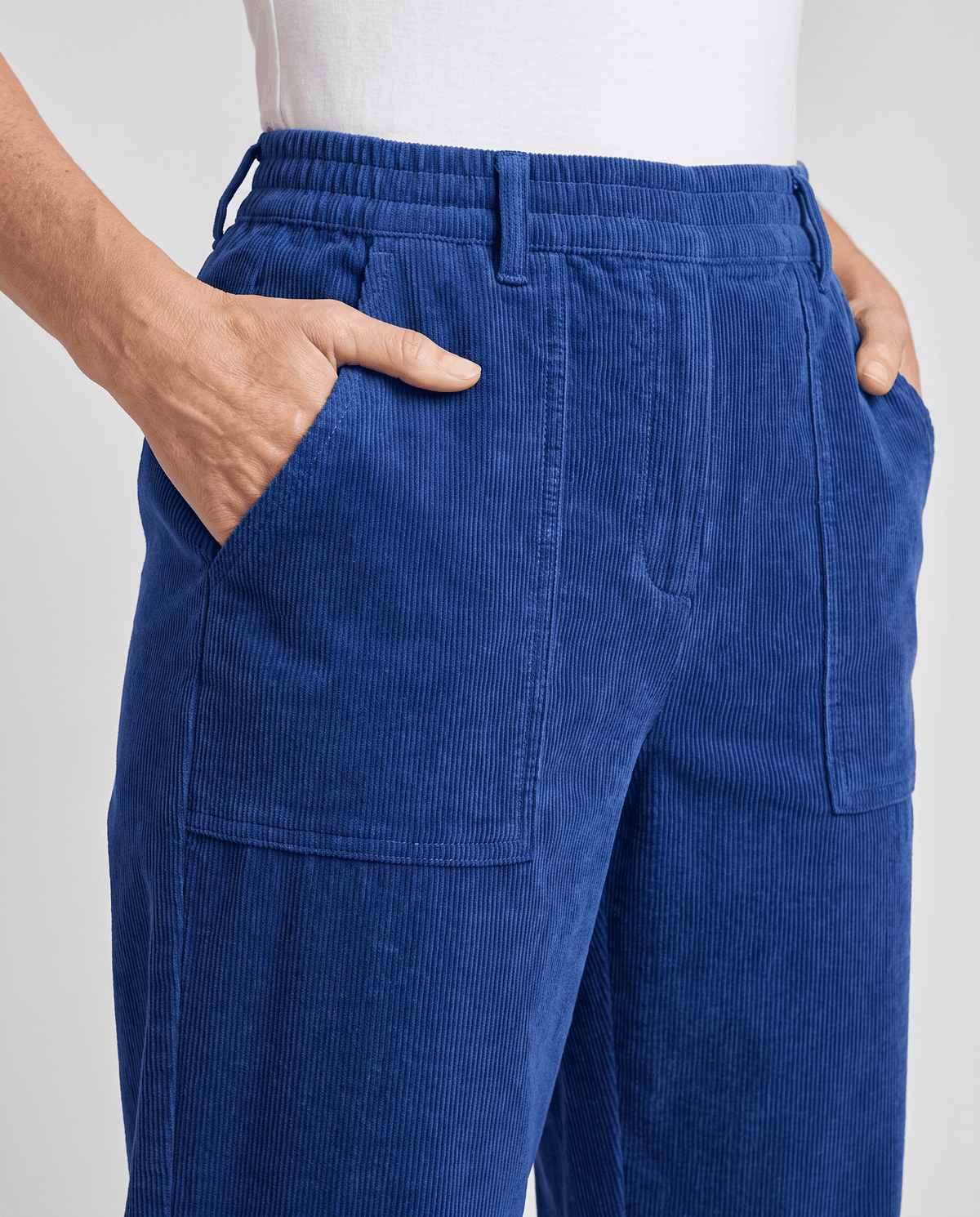 Close-up of blue corduroy front waistband with slant hand pockets and stitched patch pockets
