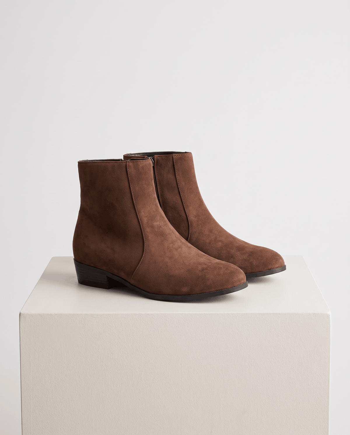 Pair of brown suede-look ankle boots displayed on a white pedestal