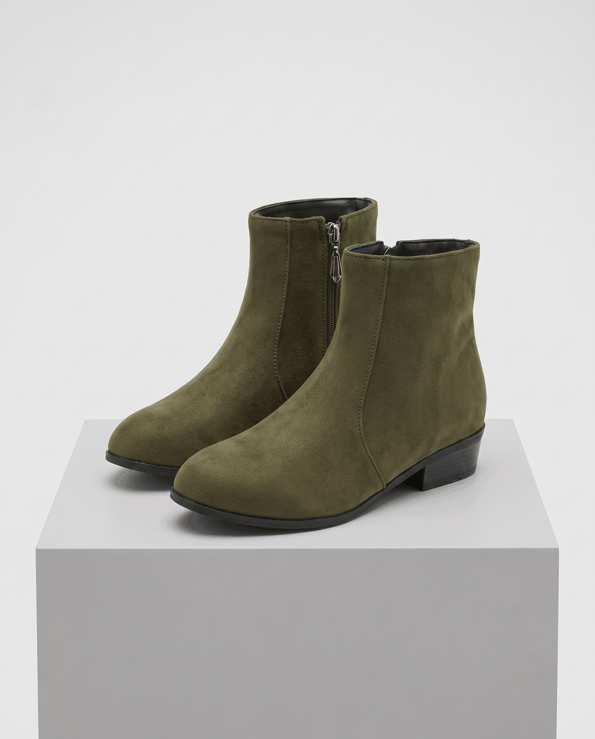 Olive green suede-look ankle boots displayed on a white pedestal