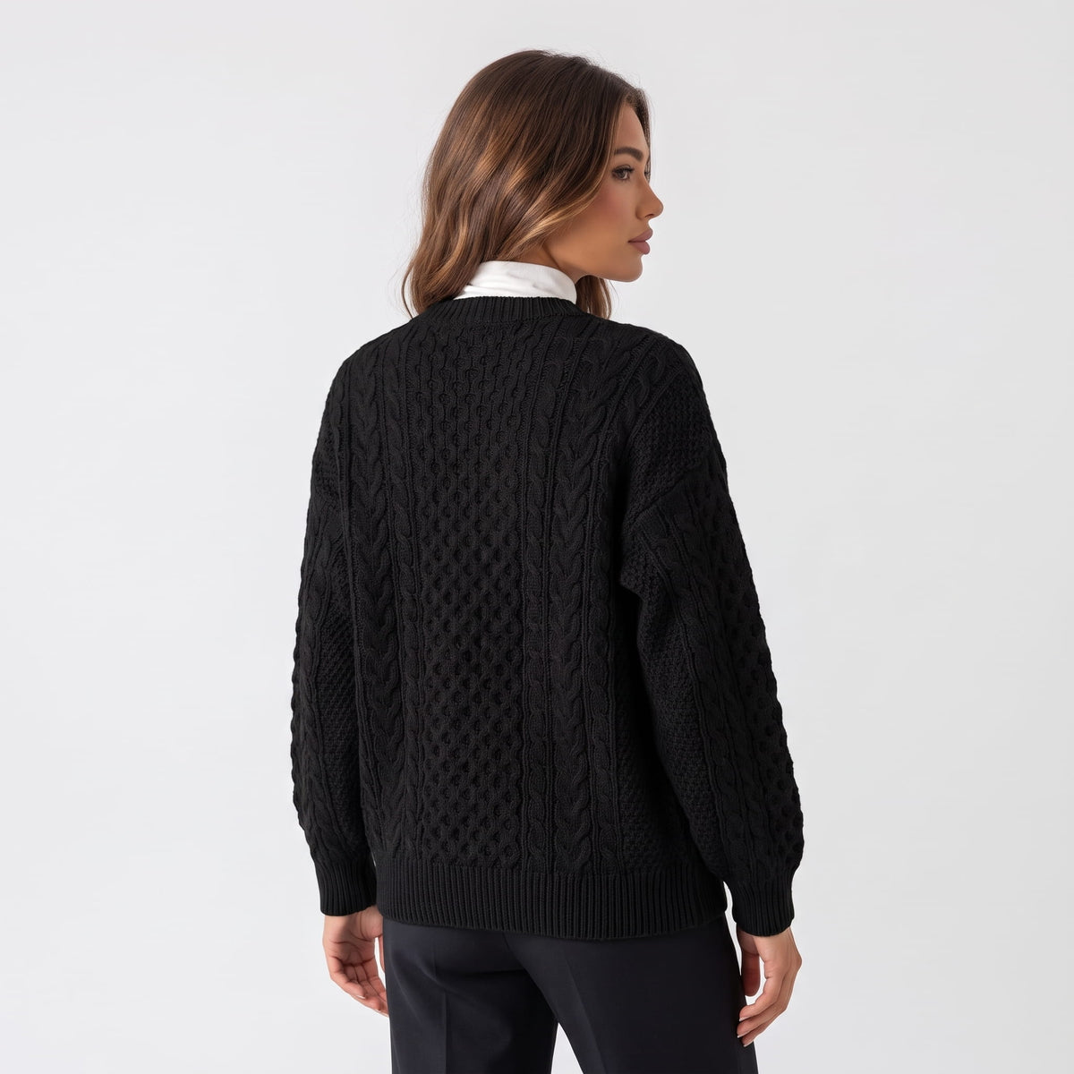 Back view of black cable-knit cardigan worn with leather trousers