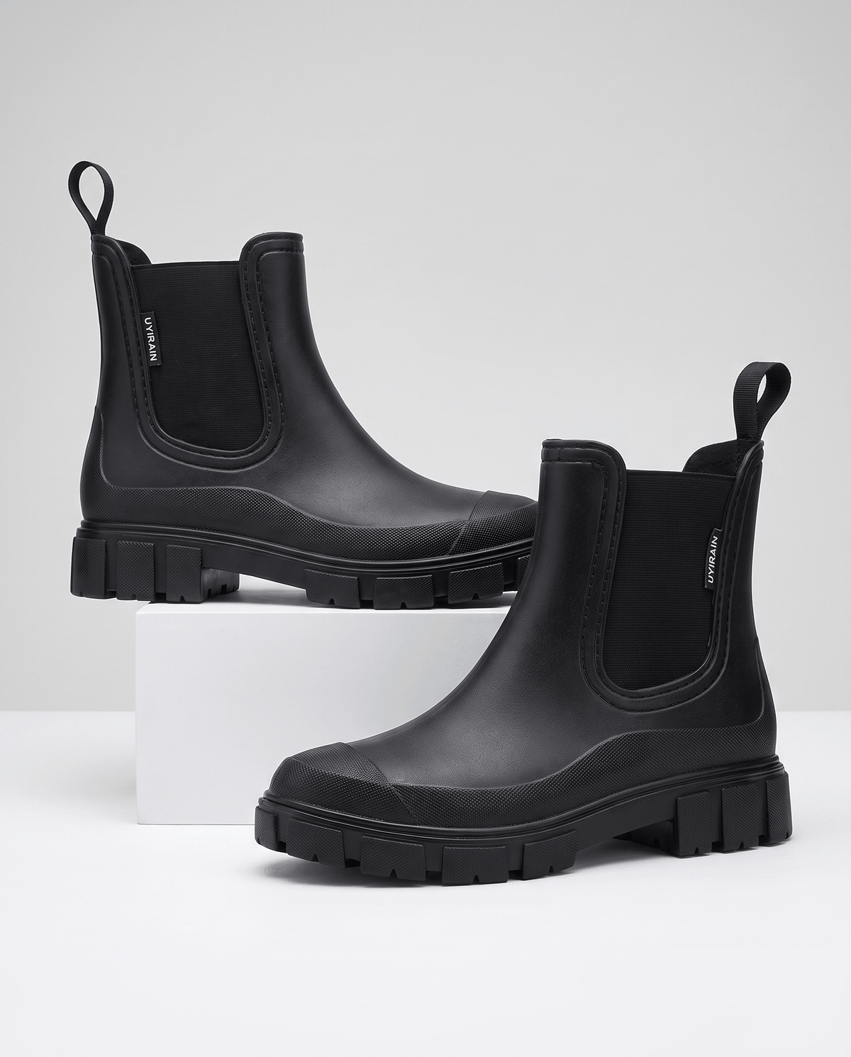 Black Chelsea-style ankle boots with chunky lug soles displayed on white blocks.