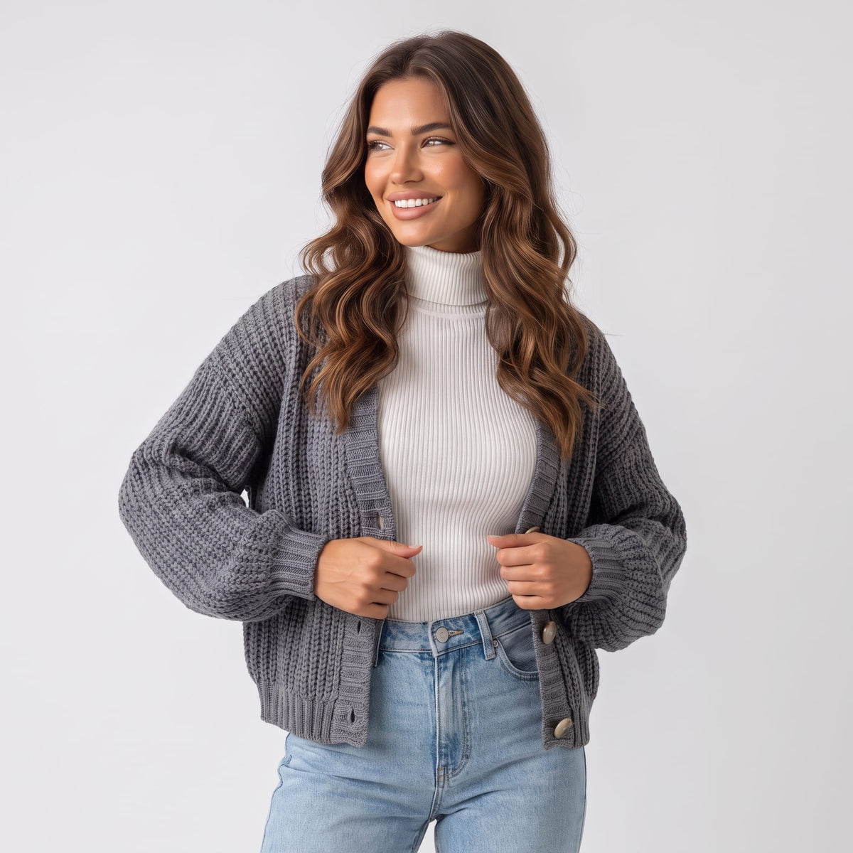 Women's gray chunky knit button cardigan worn over a white turtleneck and light blue jeans