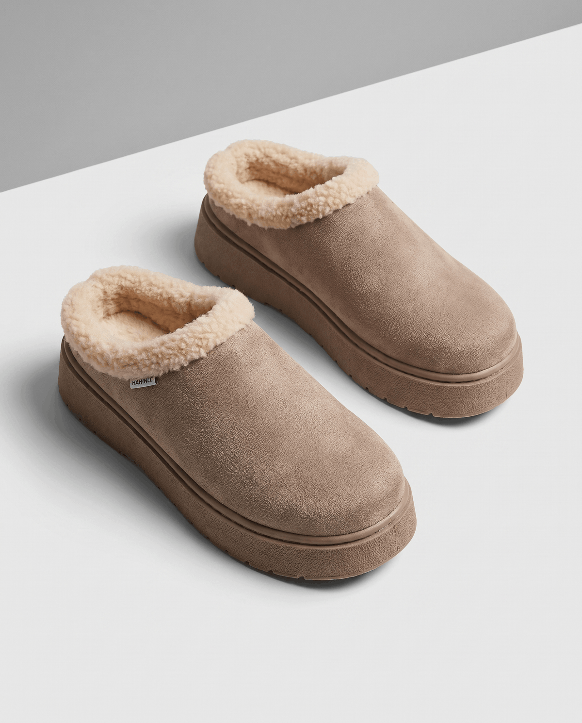 Pair of taupe slip-on slippers with a thick cream shearling-look lining and cushioned platform soles.