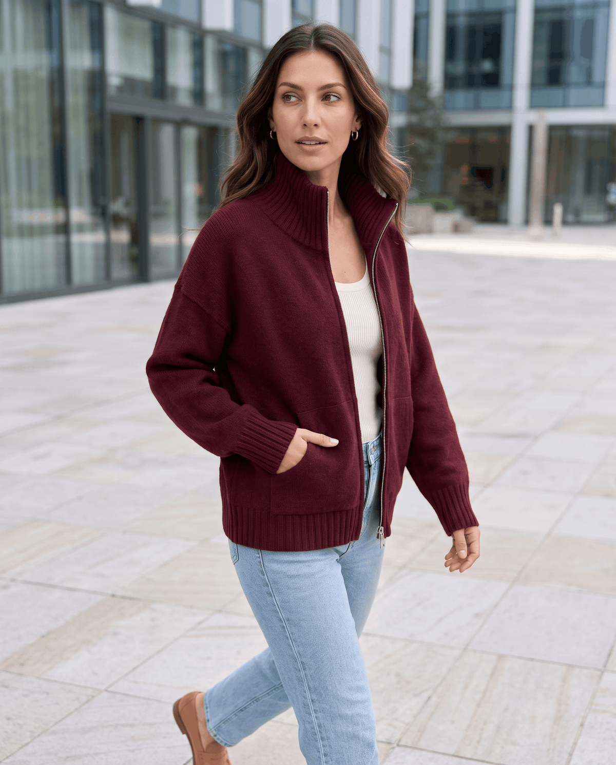 Wine red zip up cardigan styled with jeans on a city street