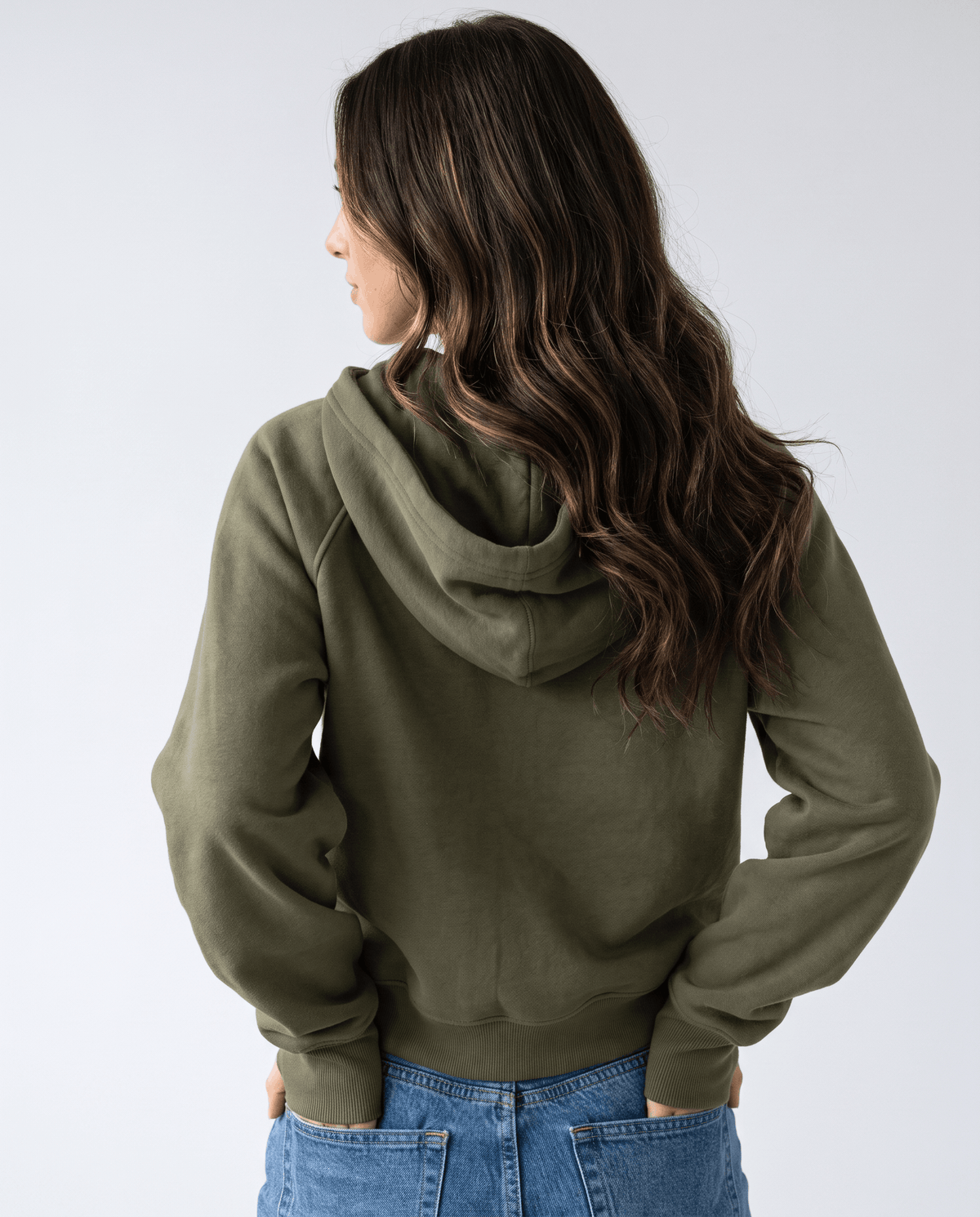 Back view of the green hooded pullover showing the hood and cropped hem over jeans