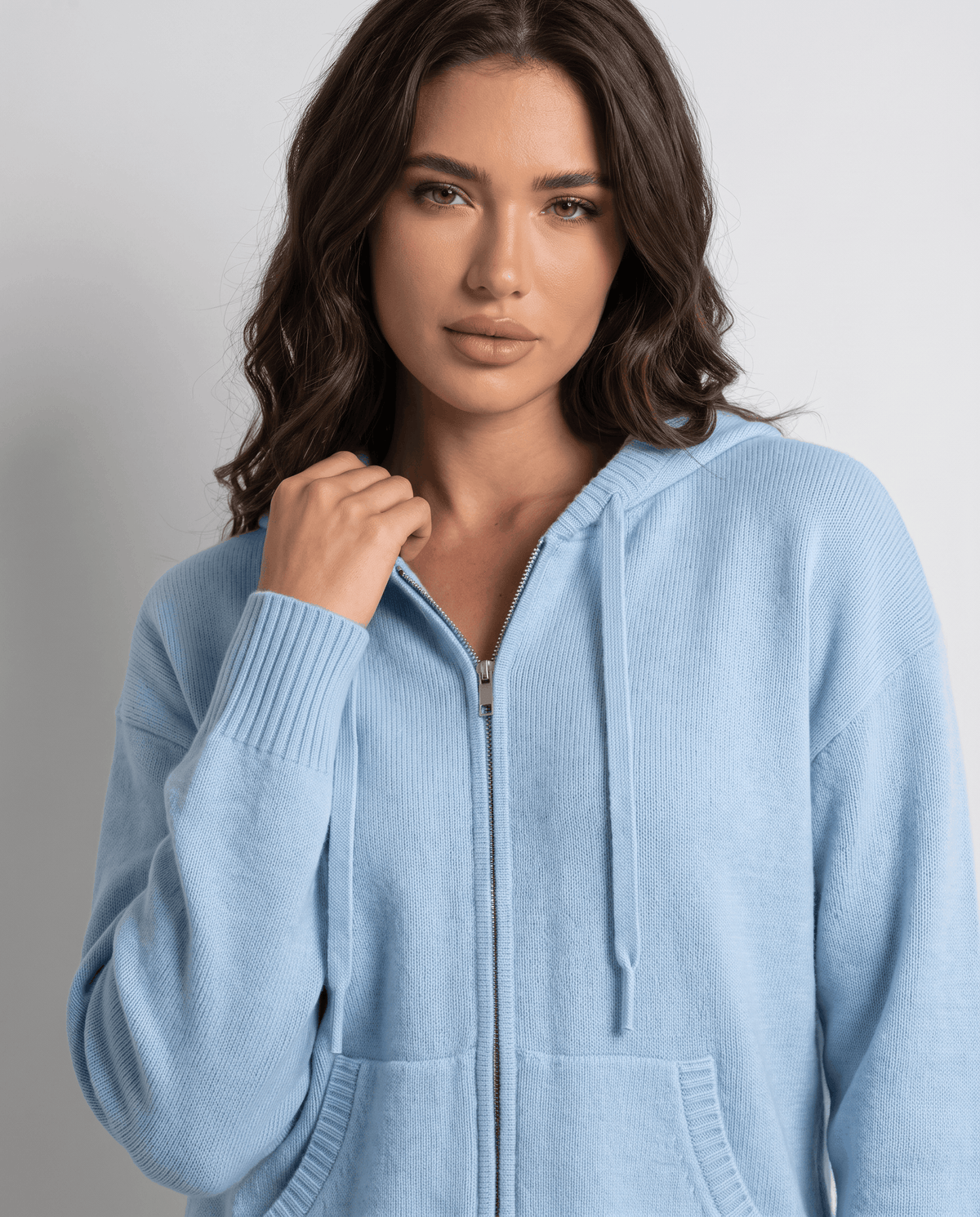 Close-up of sky blue cardigan front zip and drawstrings with a hand at the hood