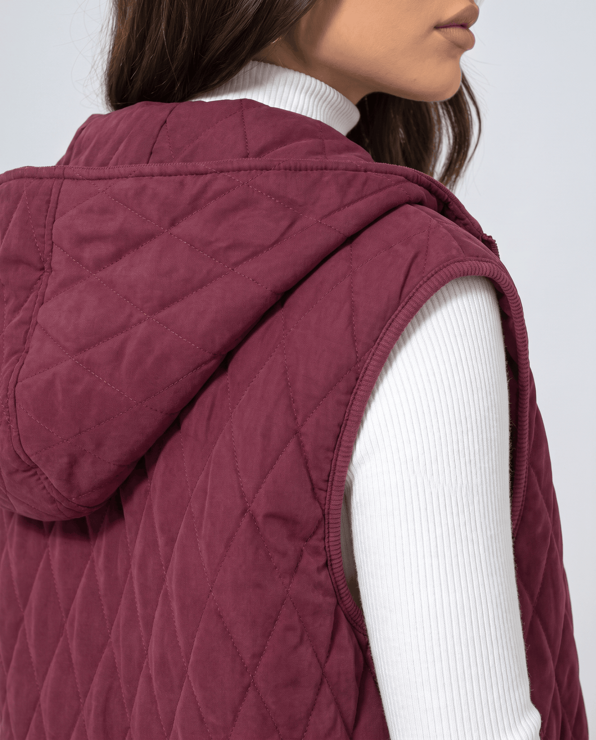 Side detail of burgundy quilted vest hood and sleeveless armhole