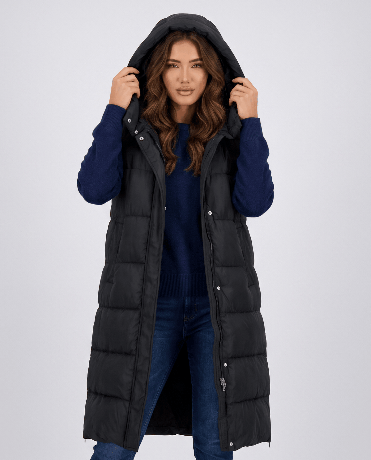 Black long quilted hooded vest with hood up worn over a navy sweater