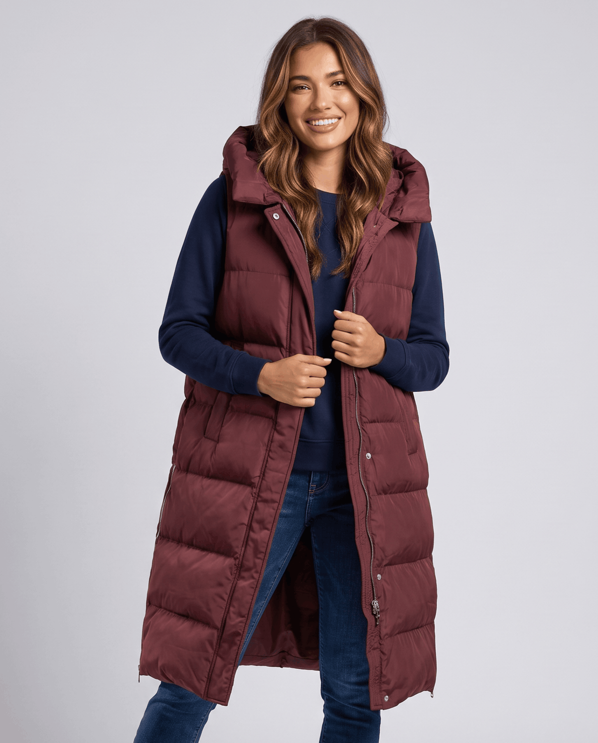 Burgundy long quilted hooded vest worn over a navy sweater and jeans