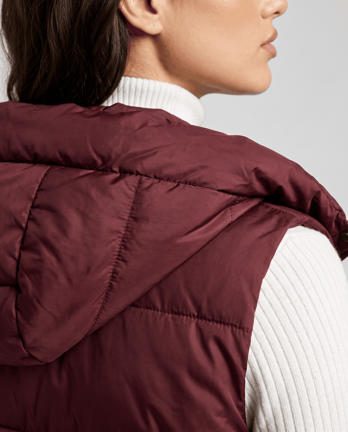 Side view of burgundy quilted vest hood and sleeveless armhole