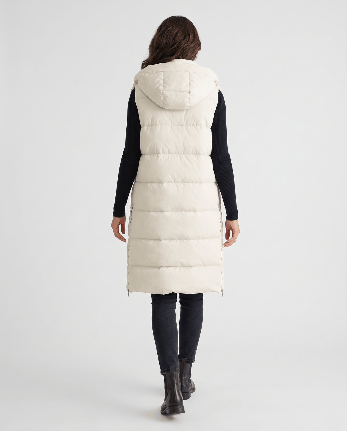 Back view of cream knee-length hooded quilted vest with black boots