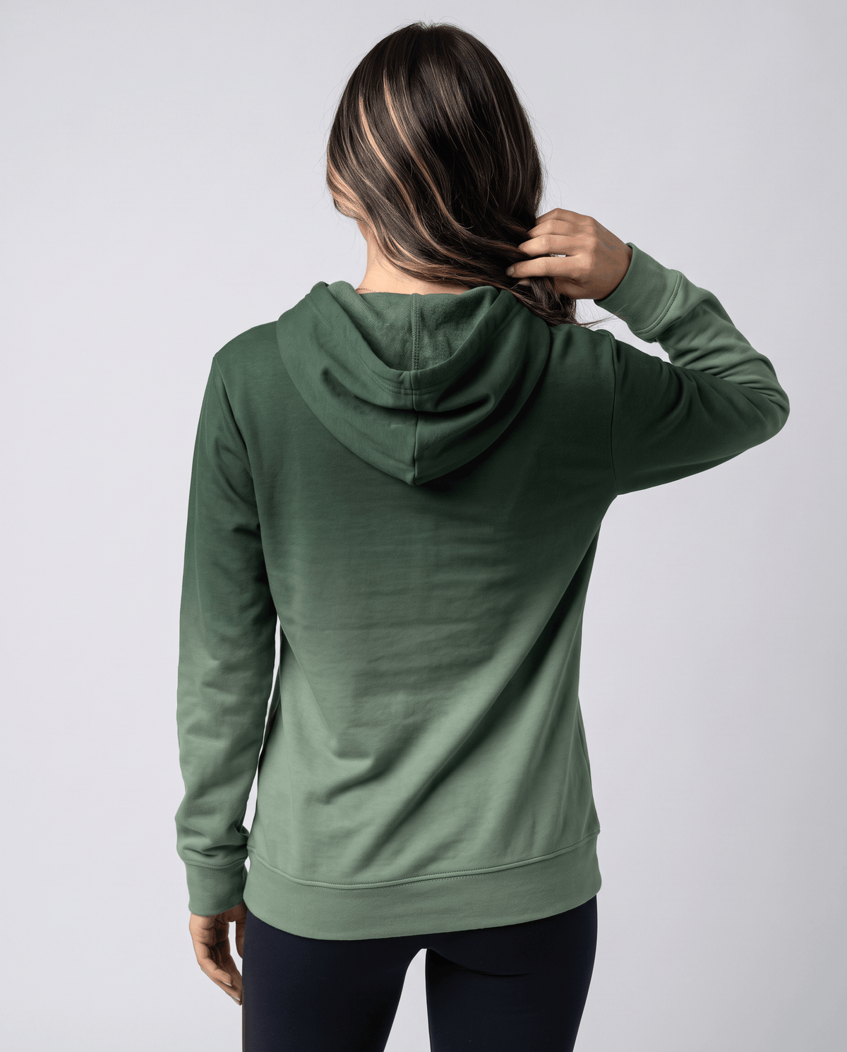 Back view of the green ombre pullover with the hood down over black leggings