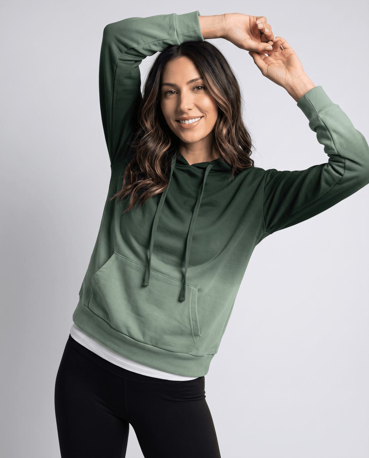 Green gradient hoodie worn with black leggings and one arm raised, front view