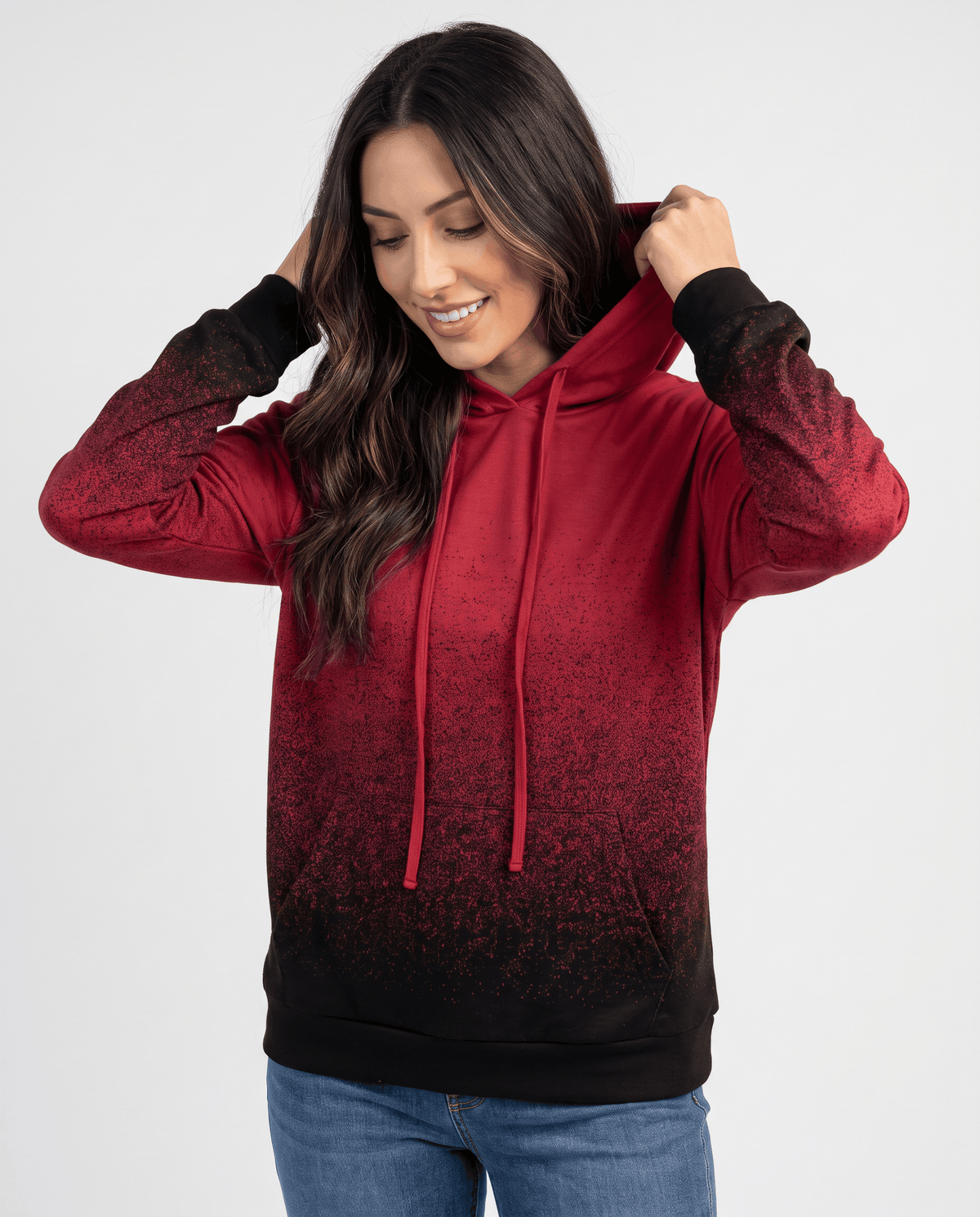 Red speckled gradient hoodie with drawstring hood worn with jeans, hands on the hood, front view