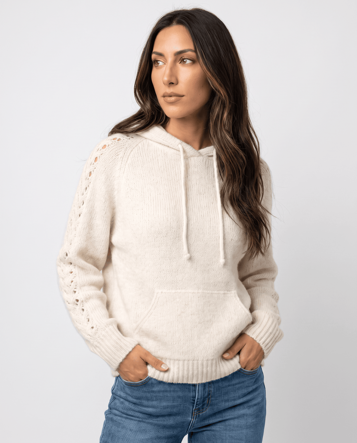 White hooded sweater with drawstring and open-stitch sleeves worn with jeans, front view