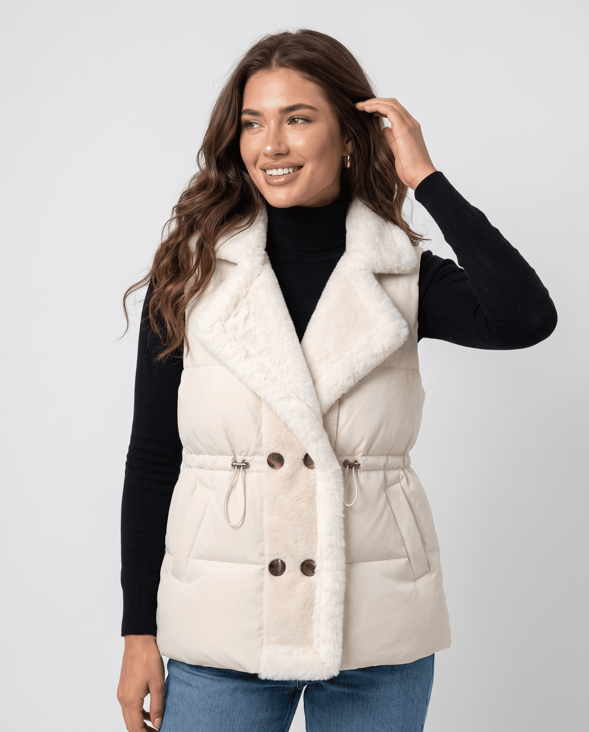 Ivory padded vest with plush collar and cinched waist worn over a black turtleneck