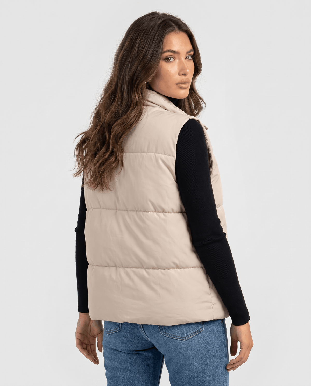 Back view of beige padded vest with horizontal sections and blue jeans