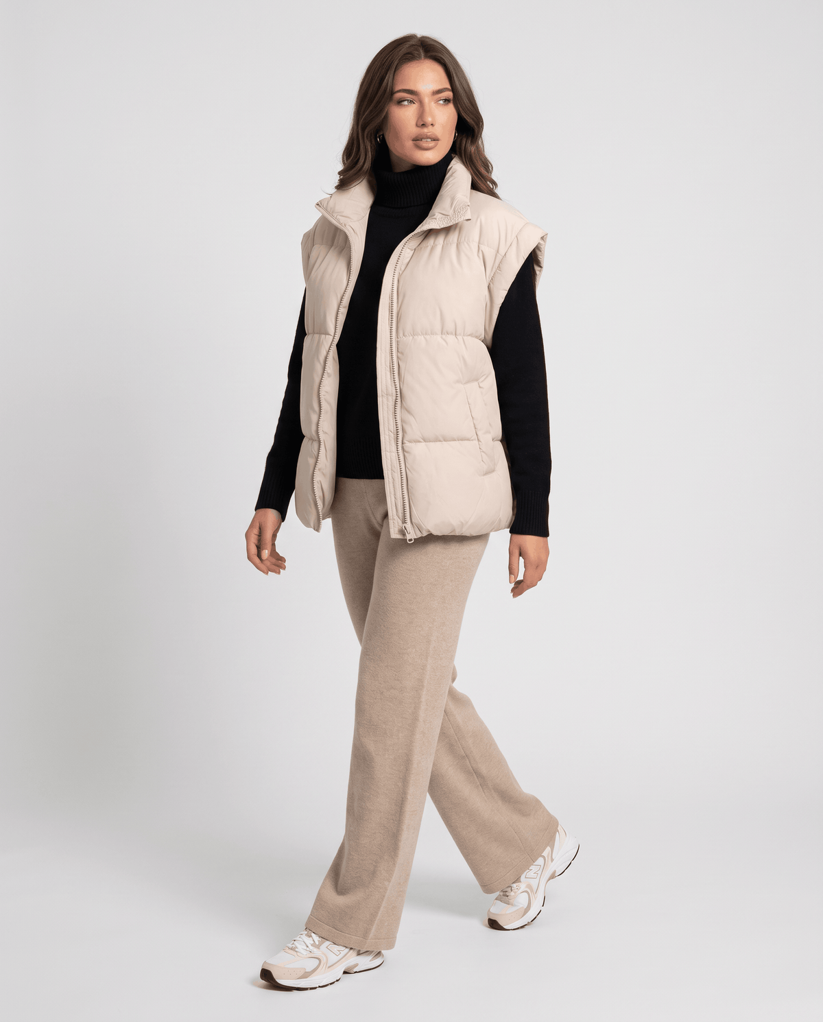 Full-length look with beige padded vest, black turtleneck and beige trousers